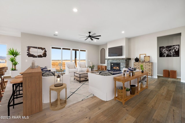 living room with hardwood / wood-style flooring, a stone fireplace, and ceiling fan