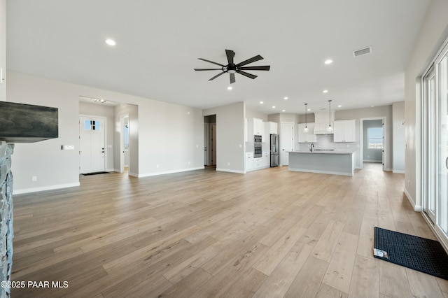 unfurnished living room with ceiling fan, a fireplace, sink, and light wood-type flooring