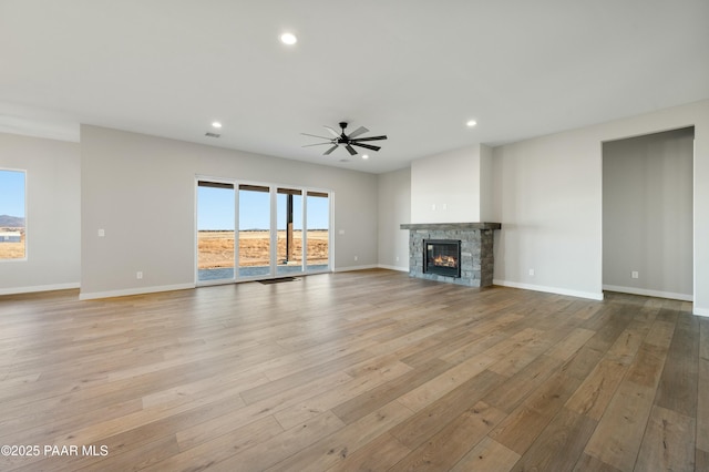 unfurnished living room featuring ceiling fan, a stone fireplace, and light wood-type flooring