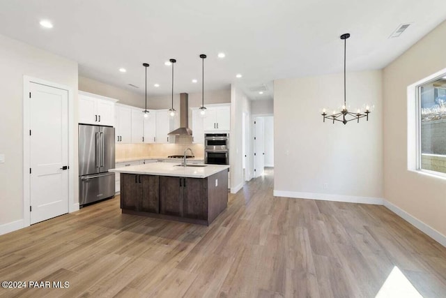 kitchen featuring decorative light fixtures, stainless steel appliances, wall chimney range hood, and light wood-type flooring