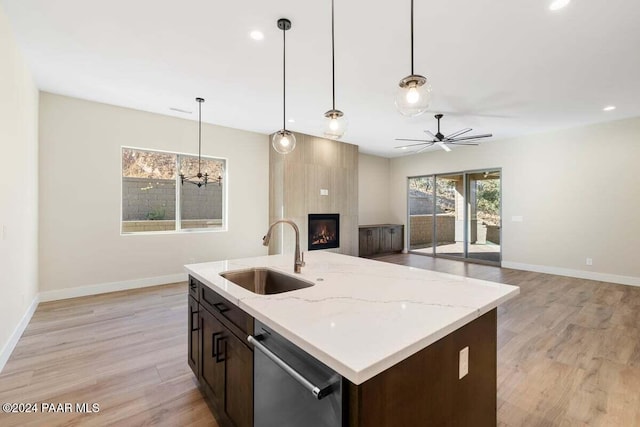 kitchen featuring sink, hanging light fixtures, stainless steel dishwasher, a center island with sink, and light wood-type flooring