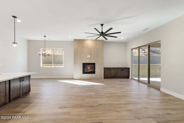 unfurnished living room featuring a fireplace, light hardwood / wood-style flooring, and ceiling fan with notable chandelier