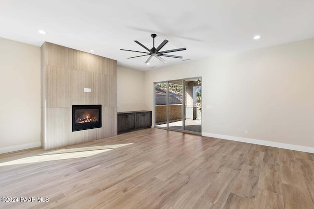 unfurnished living room featuring ceiling fan, a large fireplace, and light wood-type flooring