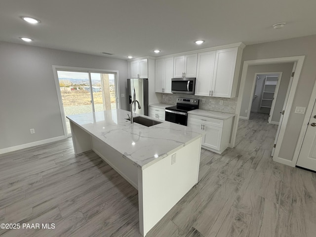 kitchen featuring white cabinetry, sink, stainless steel appliances, light stone counters, and a kitchen island with sink