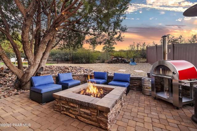 patio terrace at dusk featuring an outdoor fire pit and a grill