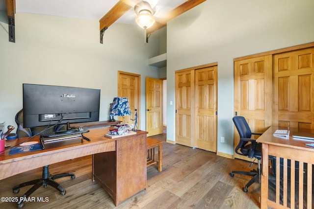 office area with light hardwood / wood-style flooring, beam ceiling, and a towering ceiling