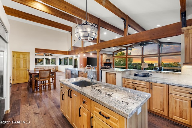 kitchen with hanging light fixtures, light stone countertops, a kitchen island with sink, and sink