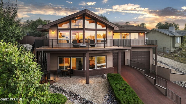 back house at dusk with a garage, a balcony, and a patio