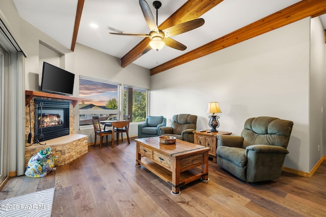 living room with hardwood / wood-style flooring, ceiling fan, a stone fireplace, and beam ceiling