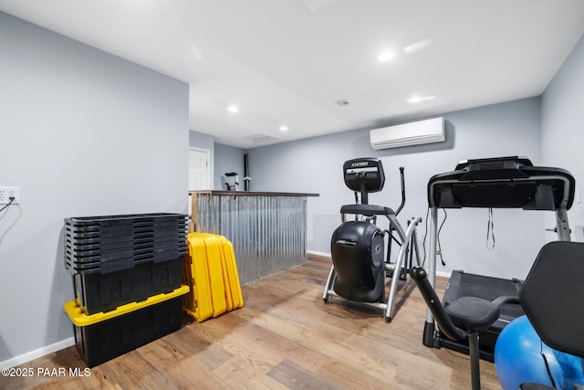 workout area featuring a wall mounted air conditioner and light hardwood / wood-style flooring