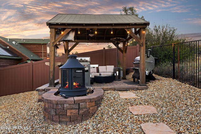 patio terrace at dusk featuring a gazebo, grilling area, ceiling fan, and an outdoor living space with a fire pit