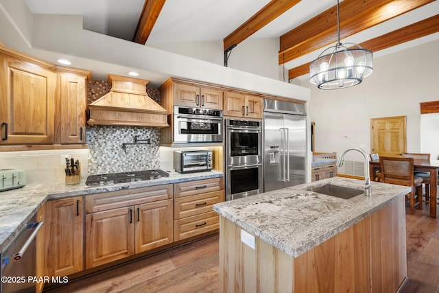 kitchen featuring sink, vaulted ceiling with beams, a center island with sink, appliances with stainless steel finishes, and custom range hood