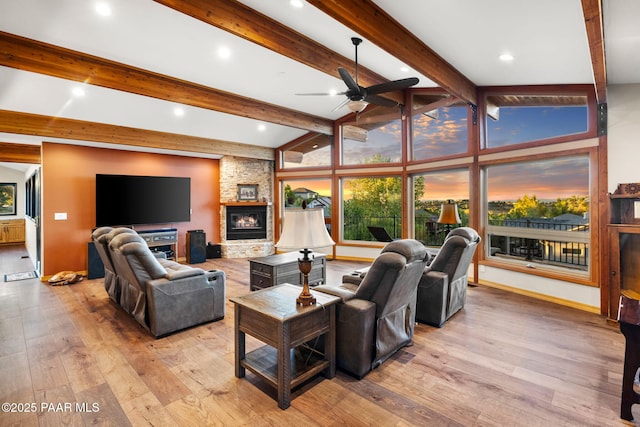 living room with lofted ceiling with beams, ceiling fan, a stone fireplace, and light hardwood / wood-style floors