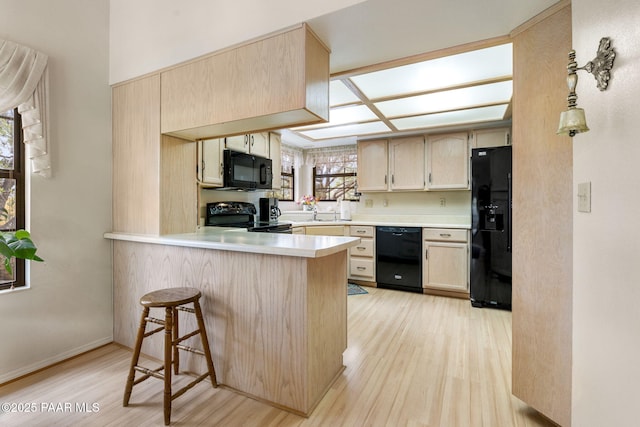 kitchen featuring light wood finished floors, a peninsula, black appliances, and light countertops