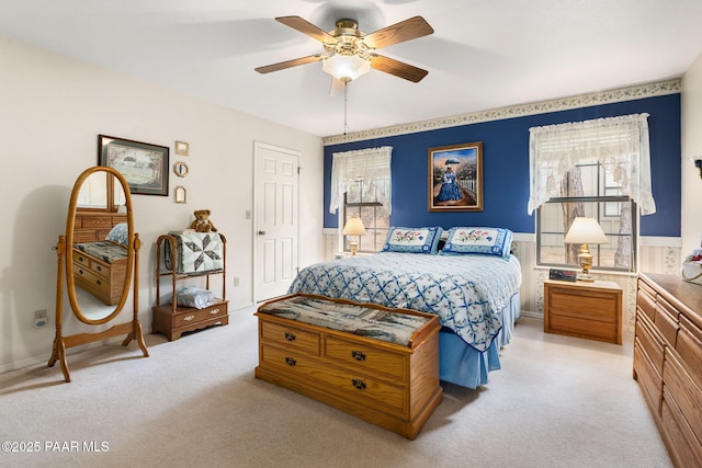 bedroom featuring a wainscoted wall, light carpet, and ceiling fan