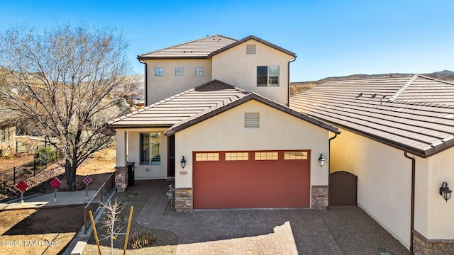 view of front of property featuring decorative driveway, stucco siding, an attached garage, stone siding, and a tiled roof