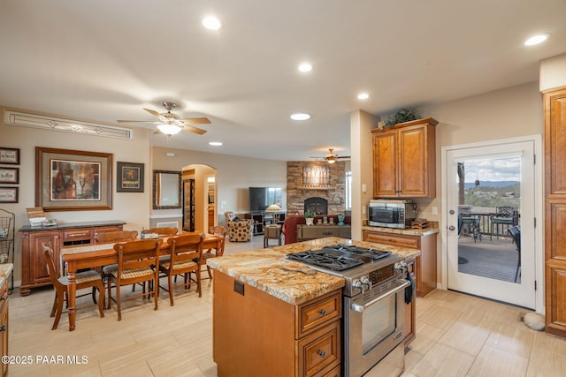 4995 Cactus Pl, Prescott, AZ 86301 - kitchen featuring stainless steel appliances, a ceiling fan, a fireplace, arched walkways, and a center island