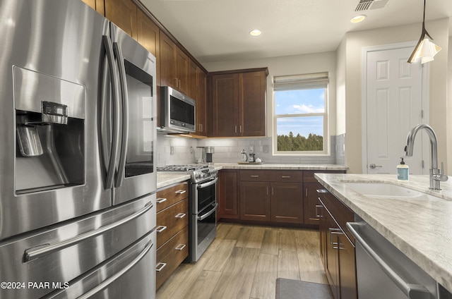 kitchen with sink, hanging light fixtures, decorative backsplash, appliances with stainless steel finishes, and light wood-type flooring