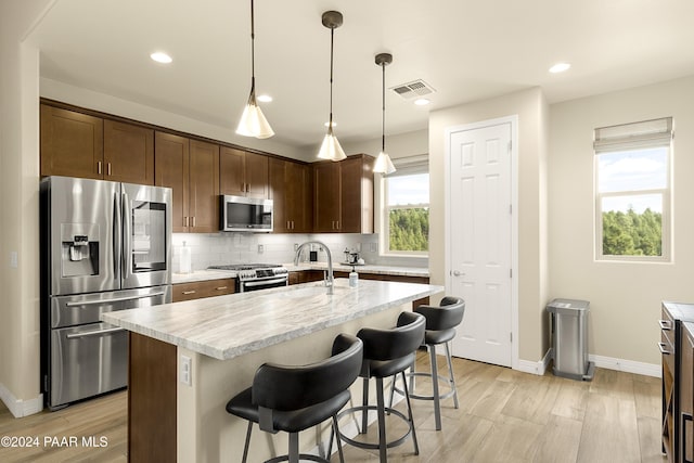 kitchen with dark brown cabinetry, stainless steel appliances, light hardwood / wood-style flooring, decorative light fixtures, and a kitchen island with sink