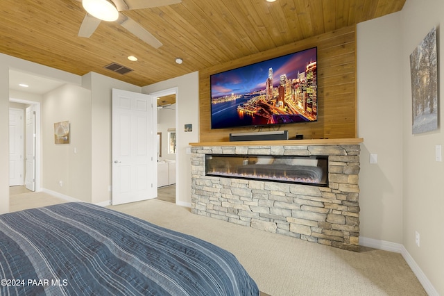 bedroom featuring a stone fireplace, light carpet, ceiling fan, and wooden ceiling