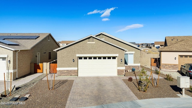 ranch-style house featuring decorative driveway, stucco siding, fence, a garage, and stone siding