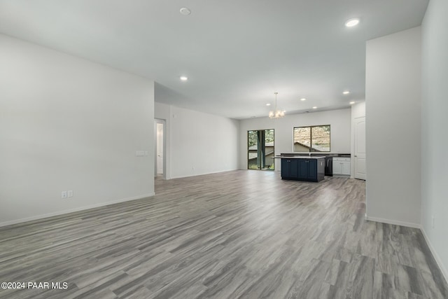 unfurnished living room with light hardwood / wood-style floors, sink, and a chandelier