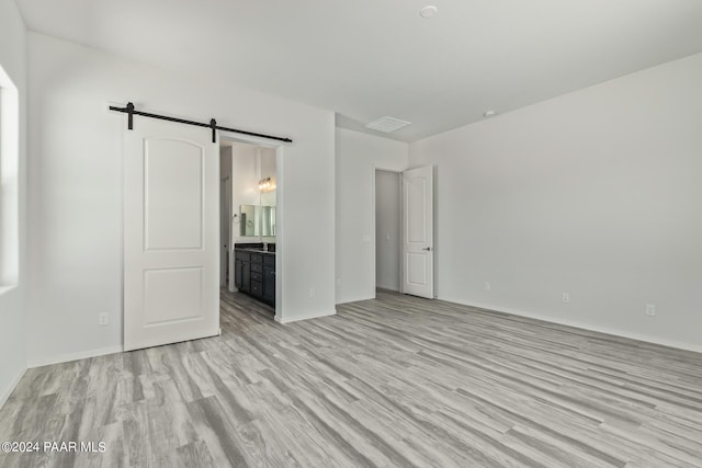 unfurnished bedroom featuring connected bathroom, a barn door, and light wood-type flooring