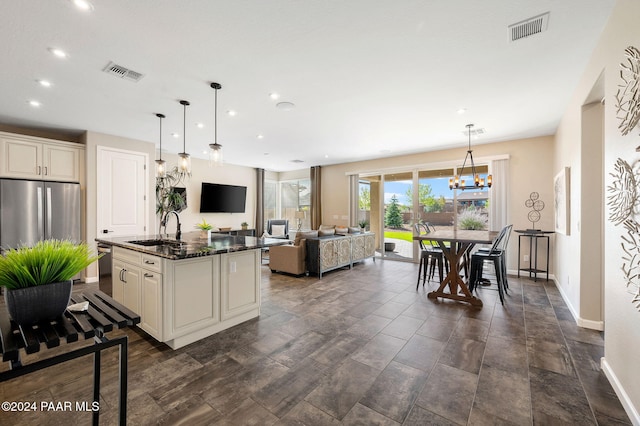 kitchen with a kitchen island with sink, dark stone counters, sink, appliances with stainless steel finishes, and decorative light fixtures