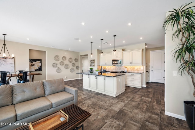 kitchen featuring sink, an inviting chandelier, backsplash, pendant lighting, and a center island with sink