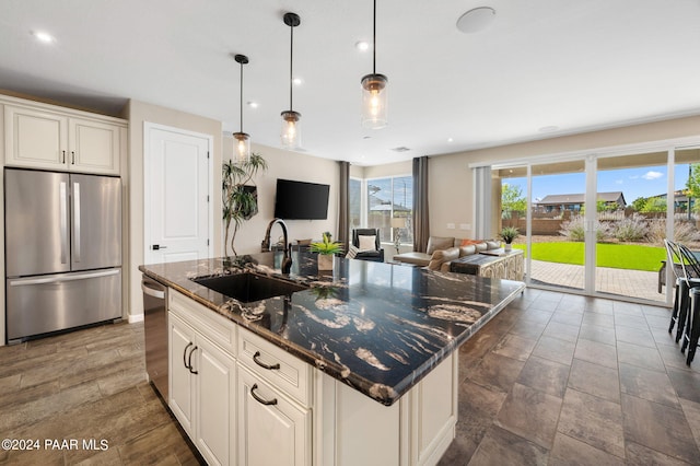 kitchen featuring appliances with stainless steel finishes, sink, a center island with sink, decorative light fixtures, and dark stone countertops