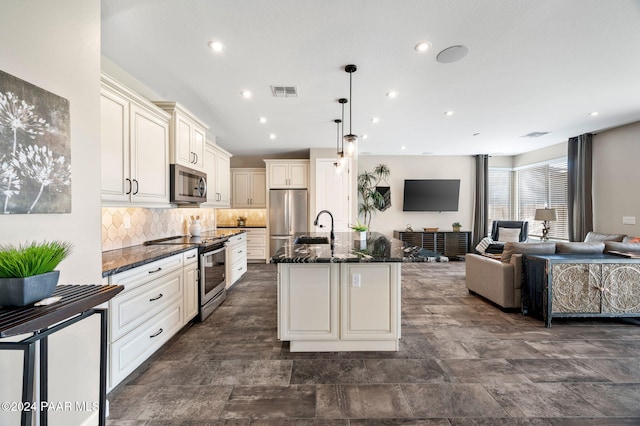 kitchen with tasteful backsplash, dark stone counters, pendant lighting, a kitchen island with sink, and appliances with stainless steel finishes