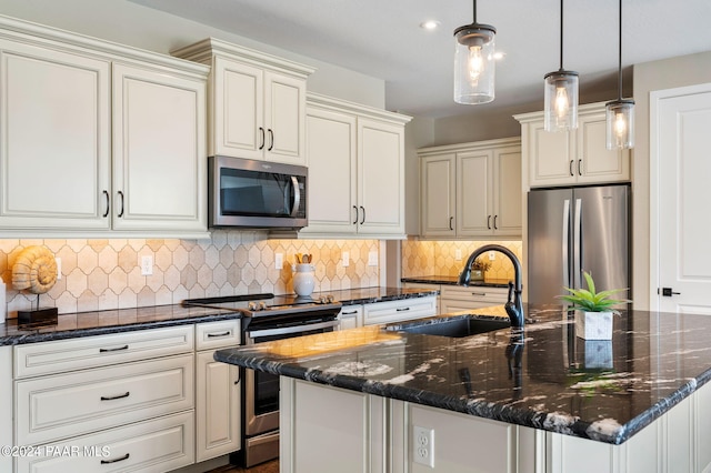 kitchen with stainless steel appliances, sink, pendant lighting, dark stone countertops, and an island with sink