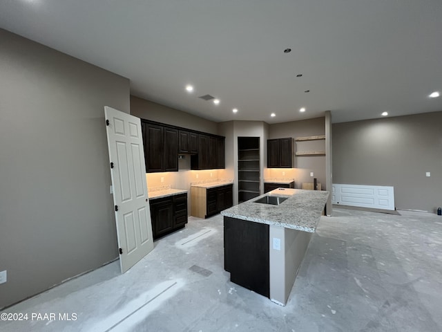 kitchen featuring sink, dark brown cabinetry, light stone countertops, and a kitchen island with sink