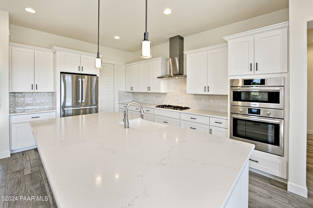 kitchen with wall chimney exhaust hood, white cabinets, a sink, and stainless steel appliances