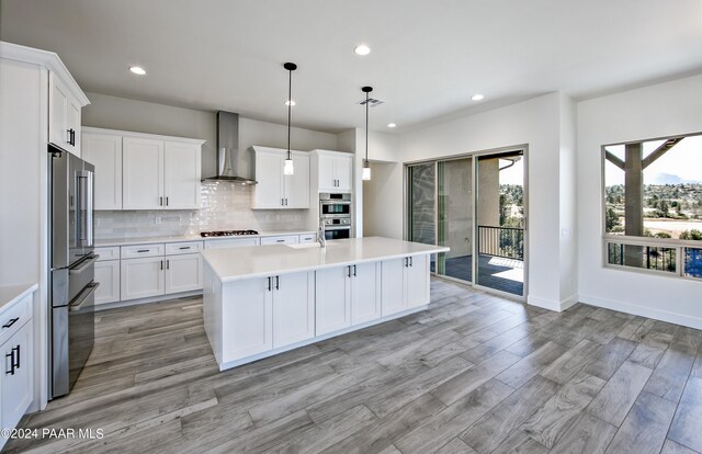 kitchen featuring light countertops, tasteful backsplash, light wood-style floors, appliances with stainless steel finishes, and wall chimney exhaust hood