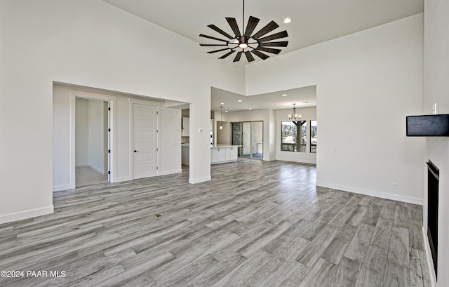 unfurnished living room featuring recessed lighting, baseboards, a high ceiling, light wood-style floors, and a notable chandelier
