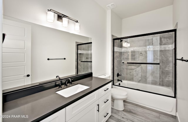 full bath with toilet, vanity, wood finished floors, visible vents, and shower / bath combination with glass door
