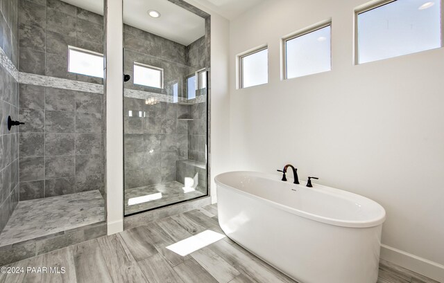 full bathroom with plenty of natural light, a freestanding tub, a stall shower, and baseboards