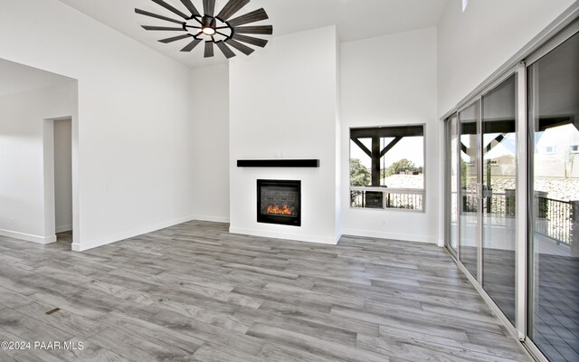 unfurnished living room with baseboards, a lit fireplace, a high ceiling, and wood finished floors
