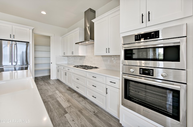 kitchen featuring light countertops, light wood finished floors, white cabinetry, stainless steel appliances, and wall chimney range hood