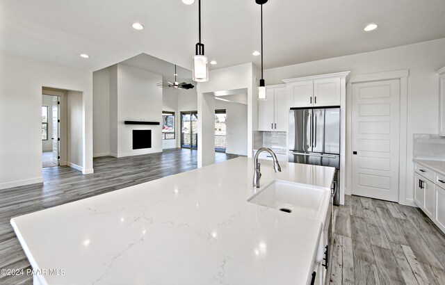 kitchen featuring white cabinetry, tasteful backsplash, a center island with sink, a sink, and light wood finished floors
