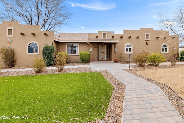 pueblo-style home featuring stucco siding and a front lawn