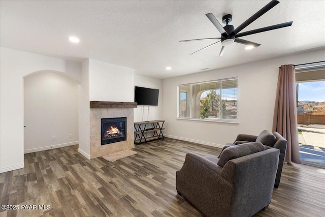 living room with dark hardwood / wood-style flooring, ceiling fan, a tiled fireplace, and a textured ceiling