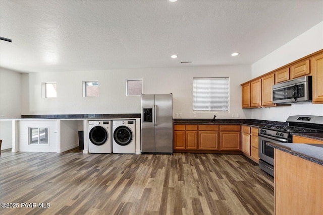 kitchen featuring a textured ceiling, dark wood-type flooring, washing machine and clothes dryer, and appliances with stainless steel finishes