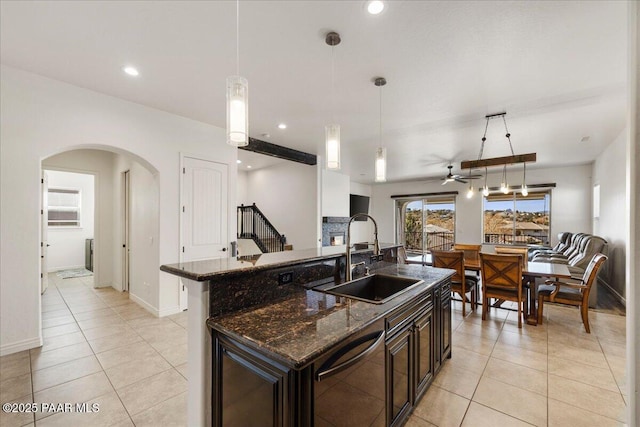 kitchen featuring decorative light fixtures, dishwasher, sink, dark stone countertops, and a kitchen island with sink