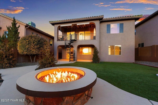 back house at dusk featuring a yard, a fire pit, a patio, and a balcony