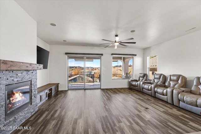 living room featuring ceiling fan, a stone fireplace, and dark hardwood / wood-style flooring