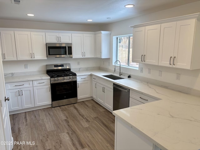 kitchen with light stone countertops, appliances with stainless steel finishes, sink, and white cabinets