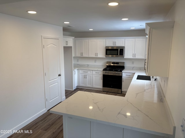 kitchen with white cabinetry, light stone counters, appliances with stainless steel finishes, dark hardwood / wood-style flooring, and kitchen peninsula