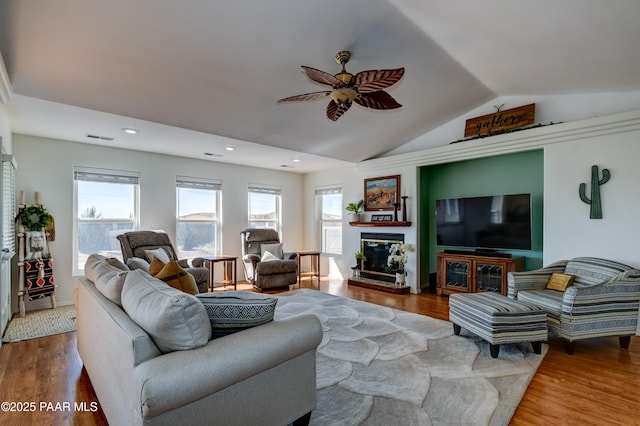 living room with a glass covered fireplace, visible vents, lofted ceiling, and wood finished floors